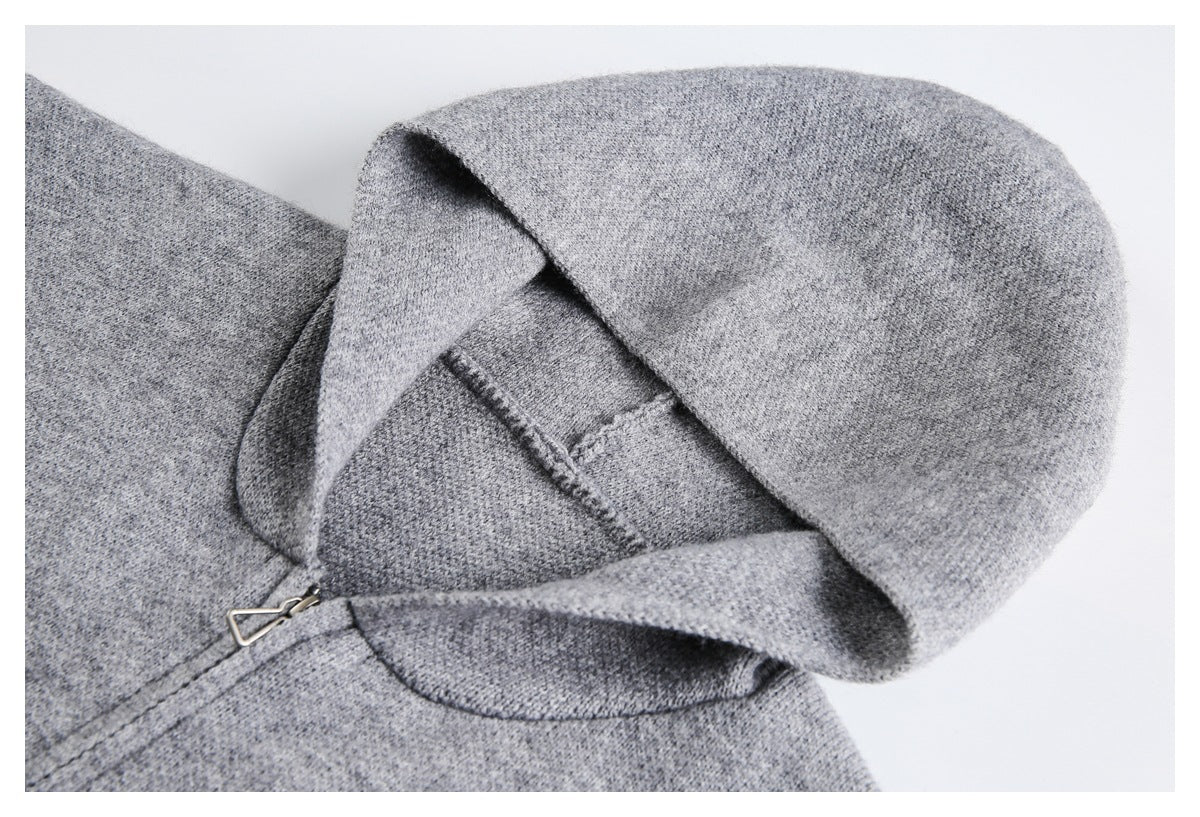 Close-up of a light gray sweater hood, showing its knit texture, seams, and a small metal zipper pull.