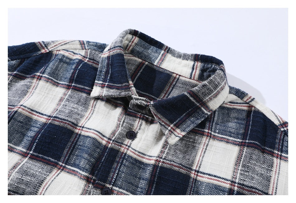 Close view of the collar and upper button placket of a white, gray and navy plaid shirt with thin red lines.