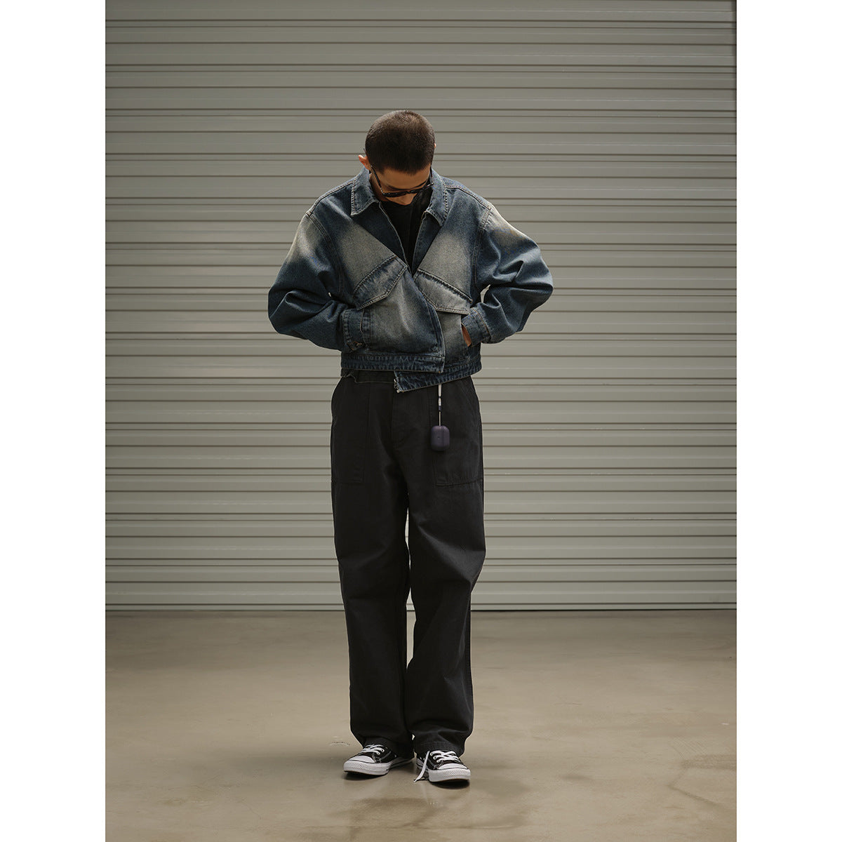 Model wearing an open faded blue denim jacket with angled flap chest pockets and loose black trousers.