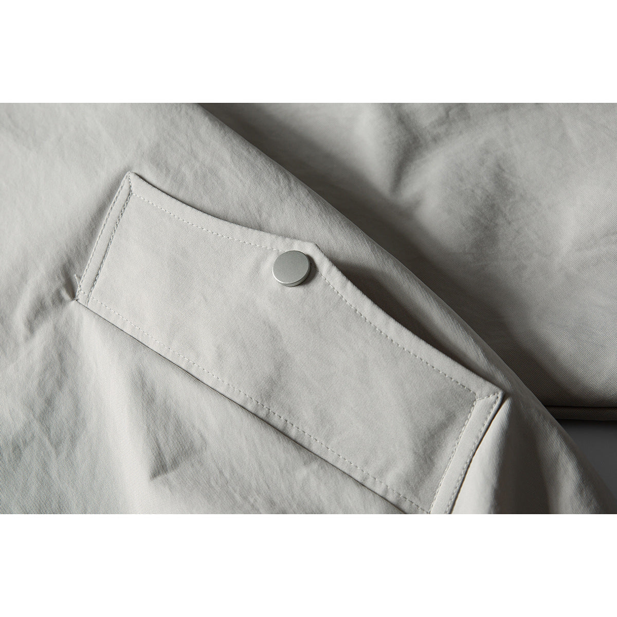 Close-up of a light gray jacket flap with a round silver snap and visible stitching.
