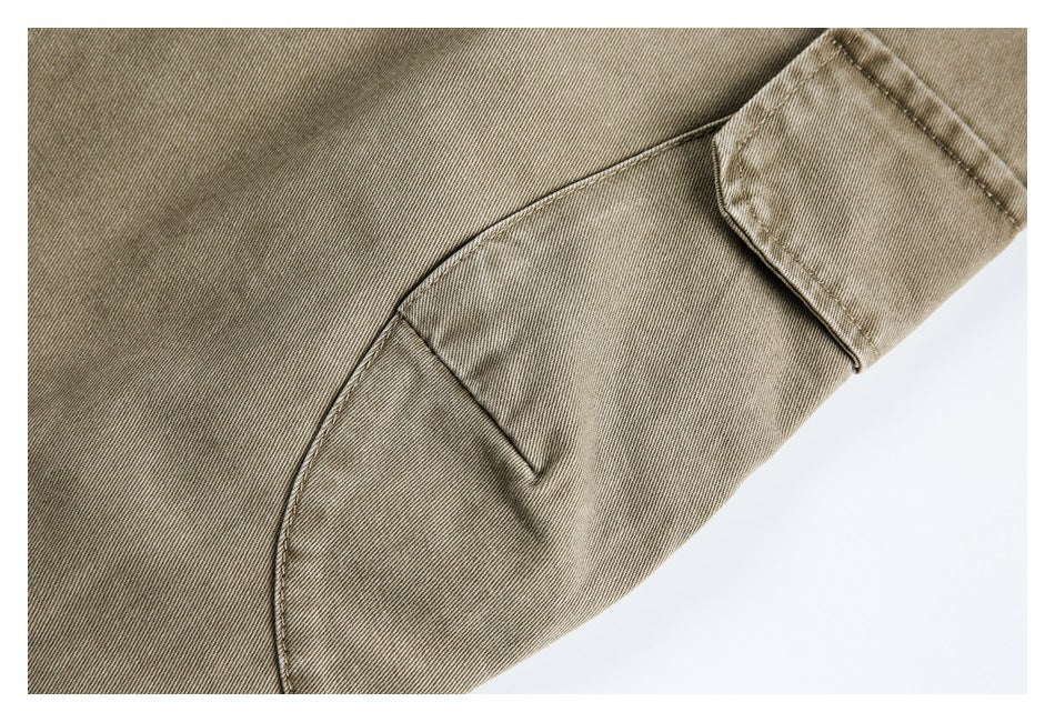 Close-up of khaki trousers showing a curved pocket opening and stitched seams.