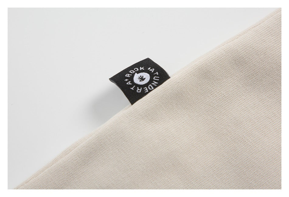 Close-up of beige knit fabric with a small black woven label bearing white lettering and a circular emblem.