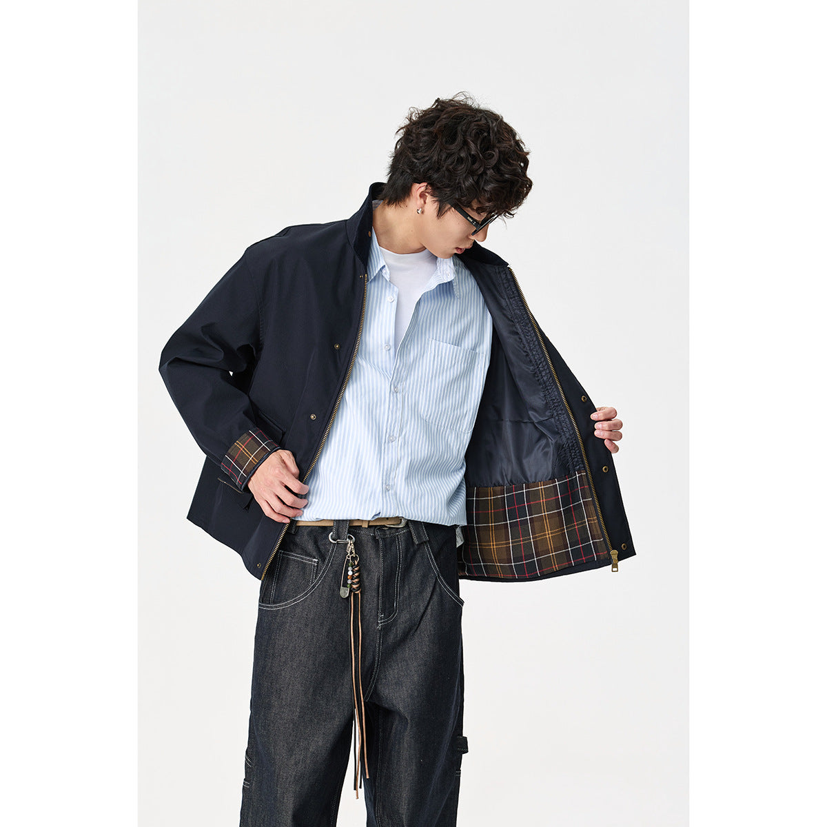 Model opens a navy jacket to show its dark lining and plaid hem panel, worn over a striped shirt.