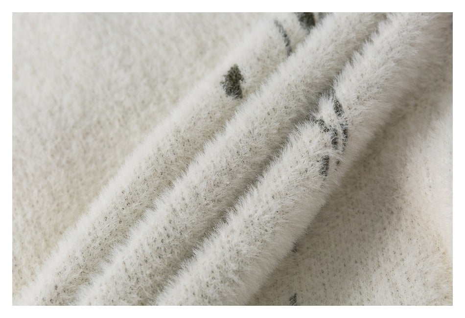 Close-up of fuzzy ivory knit with scattered dark gray pattern marks.