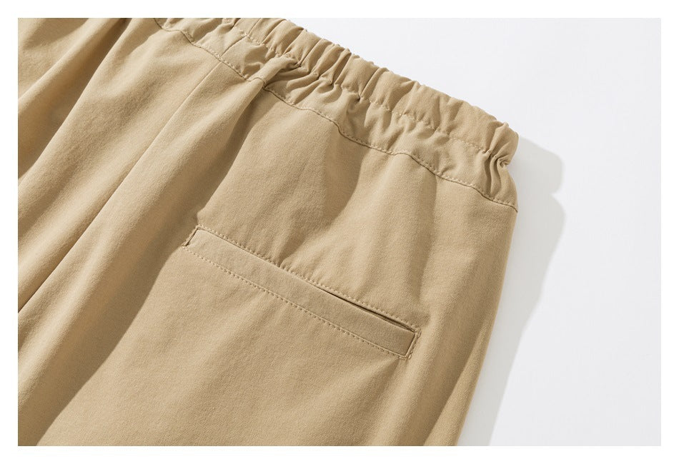 Close-up of tan pants showing the elastic back waistband and a welt pocket.