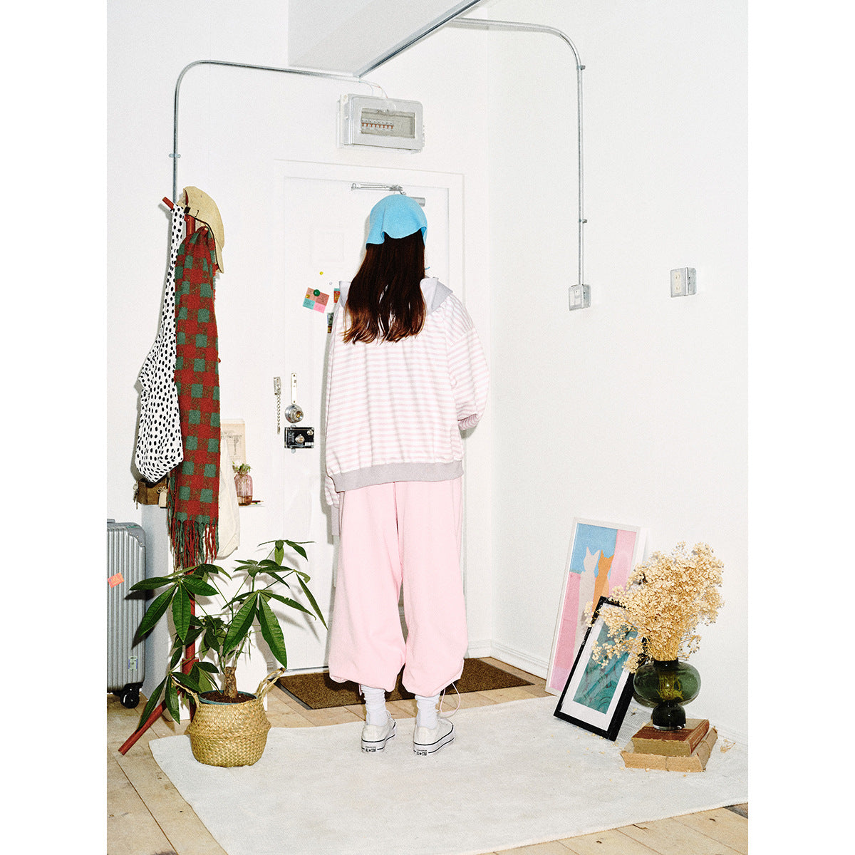 Back view of a model wearing a pale pink-and-white striped zip hoodie with gray trim and loose pink pants.