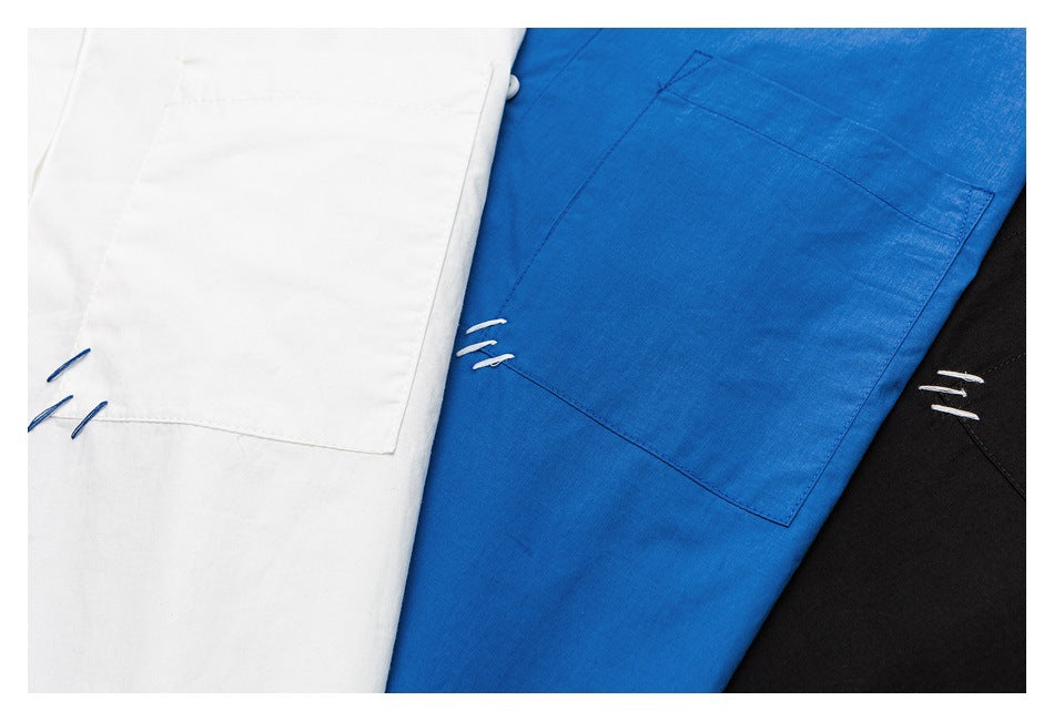 Close-up of white, bright blue, and black shirts with large chest pockets and small contrasting stitch details.