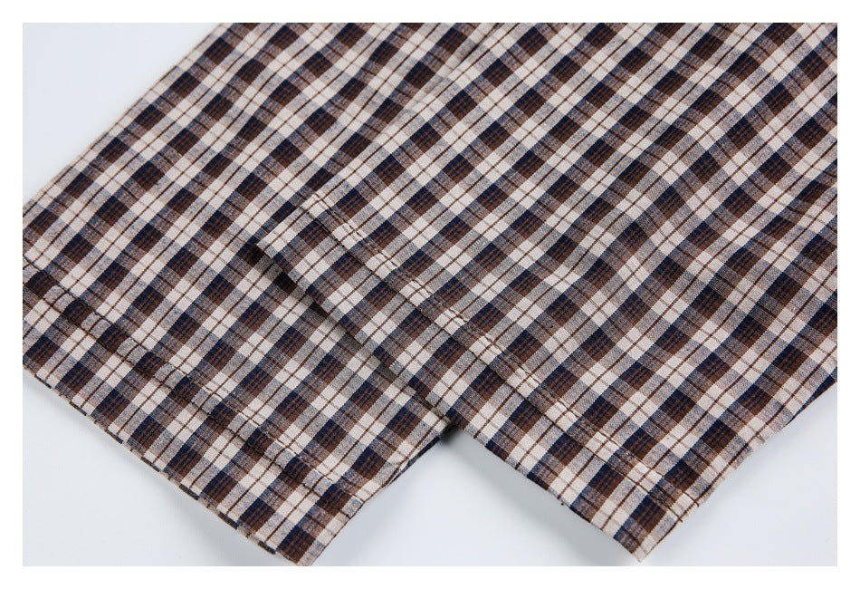 Close-up of brown, navy, and cream plaid fabric with a stitched edge and folded layers.