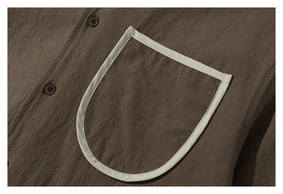 Close-up of a large patch pocket with pale trim on a brown shirt, beside two buttons.