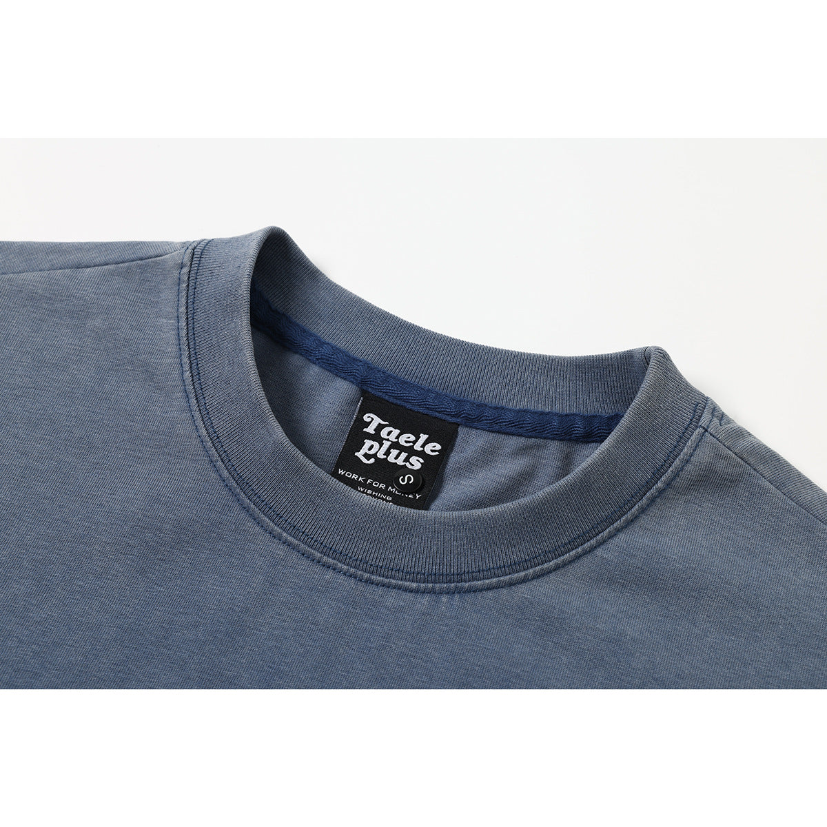 Close-up of a blue-gray shirt's ribbed crew neck and sewn black Taele Plus label.