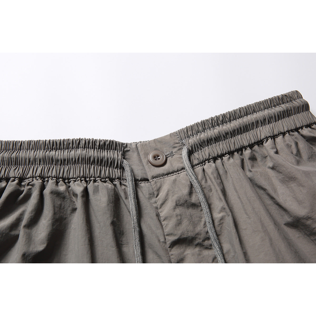 Close-up of gray shorts showing an elastic waistband, drawstring, button closure, and fly.