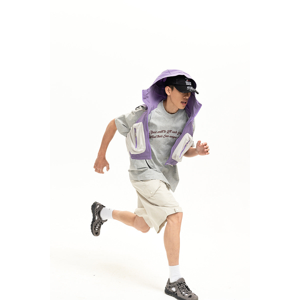 Model wearing a lavender hooded utility vest over a gray T-shirt with cream shorts.