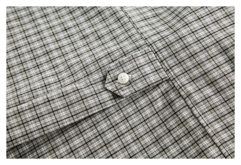 Close-up of gray plaid garment fabric with a white button on a narrow button tab.