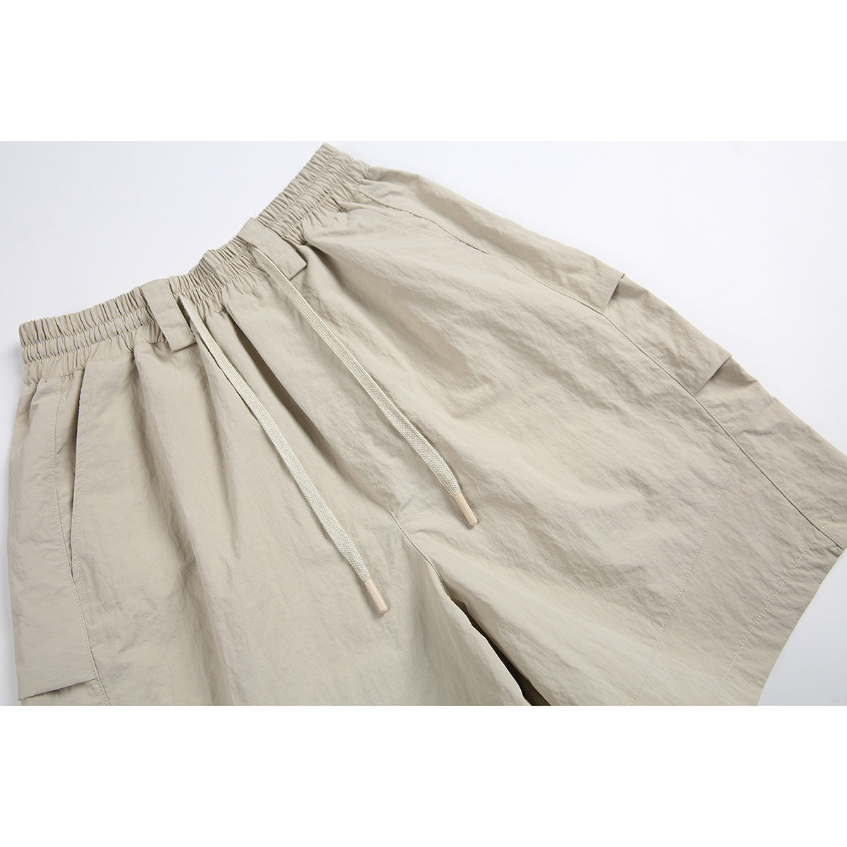 Close-up of beige shorts showing the elastic waistband, belt loops, drawstrings, and front pocket.