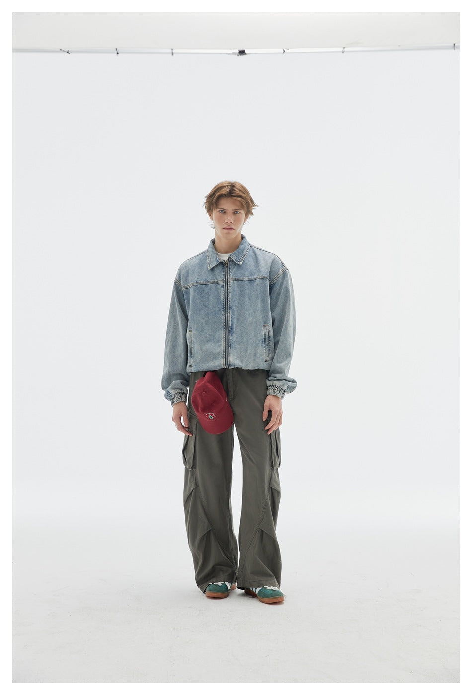 Model wearing gray-green wide-leg cargo pants with a light denim jacket and red cap, front view