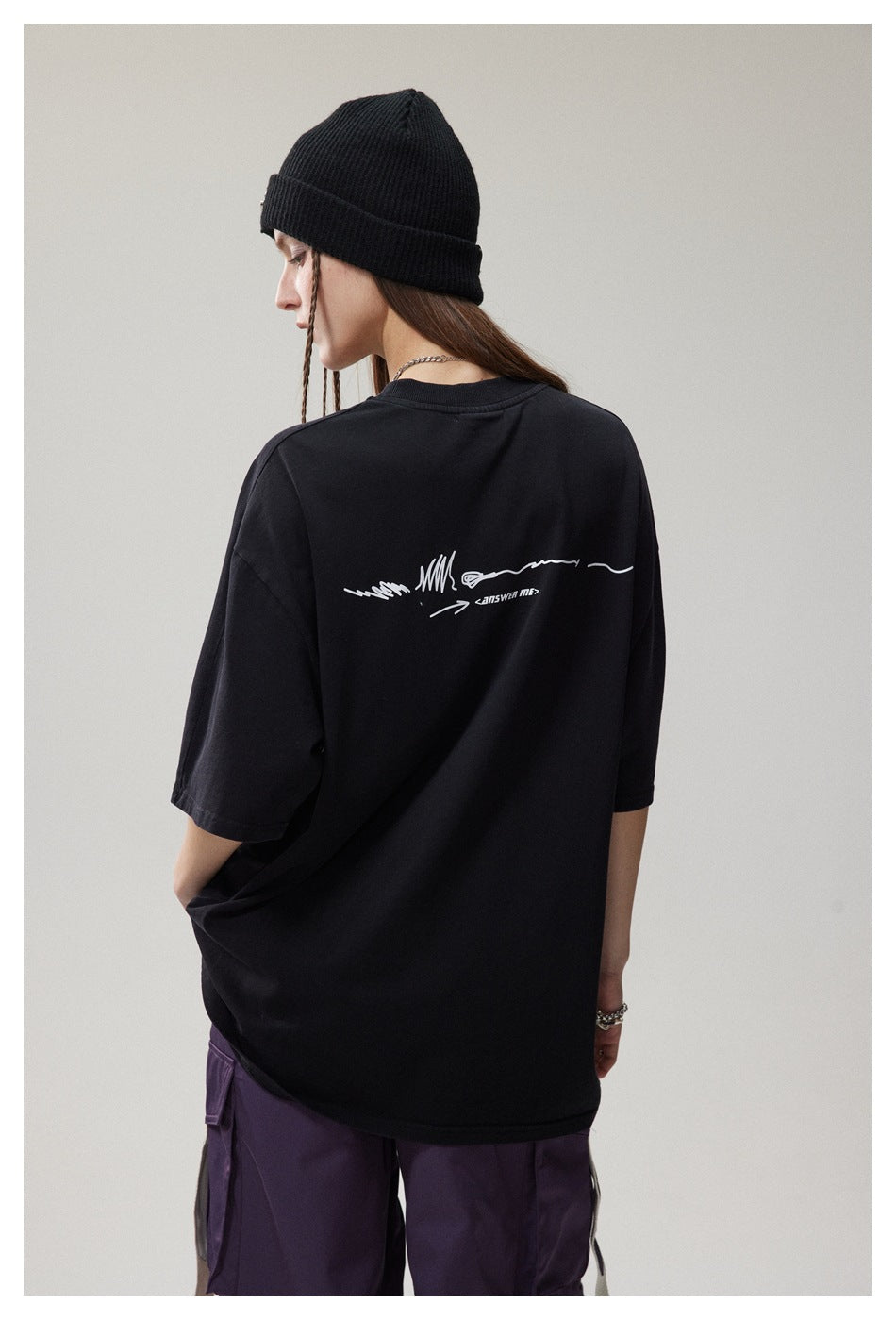 Model shown from behind in an oversized black T-shirt with a small white back graphic and purple cargo pants.