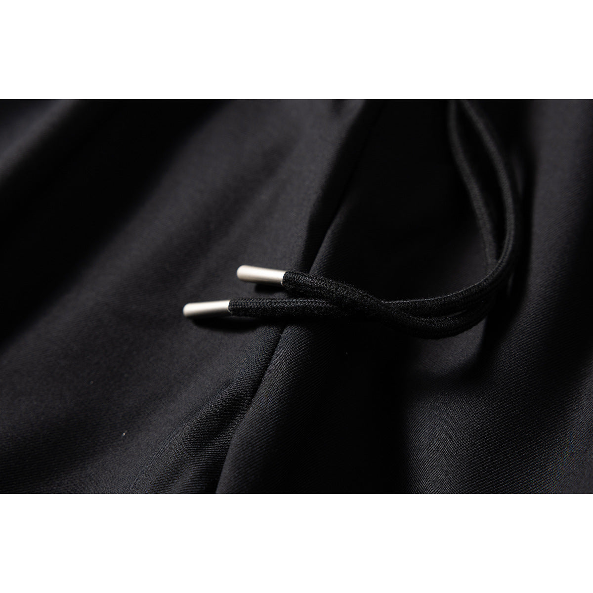 Close-up of black trouser drawstring with silver-colored tips against the fabric.