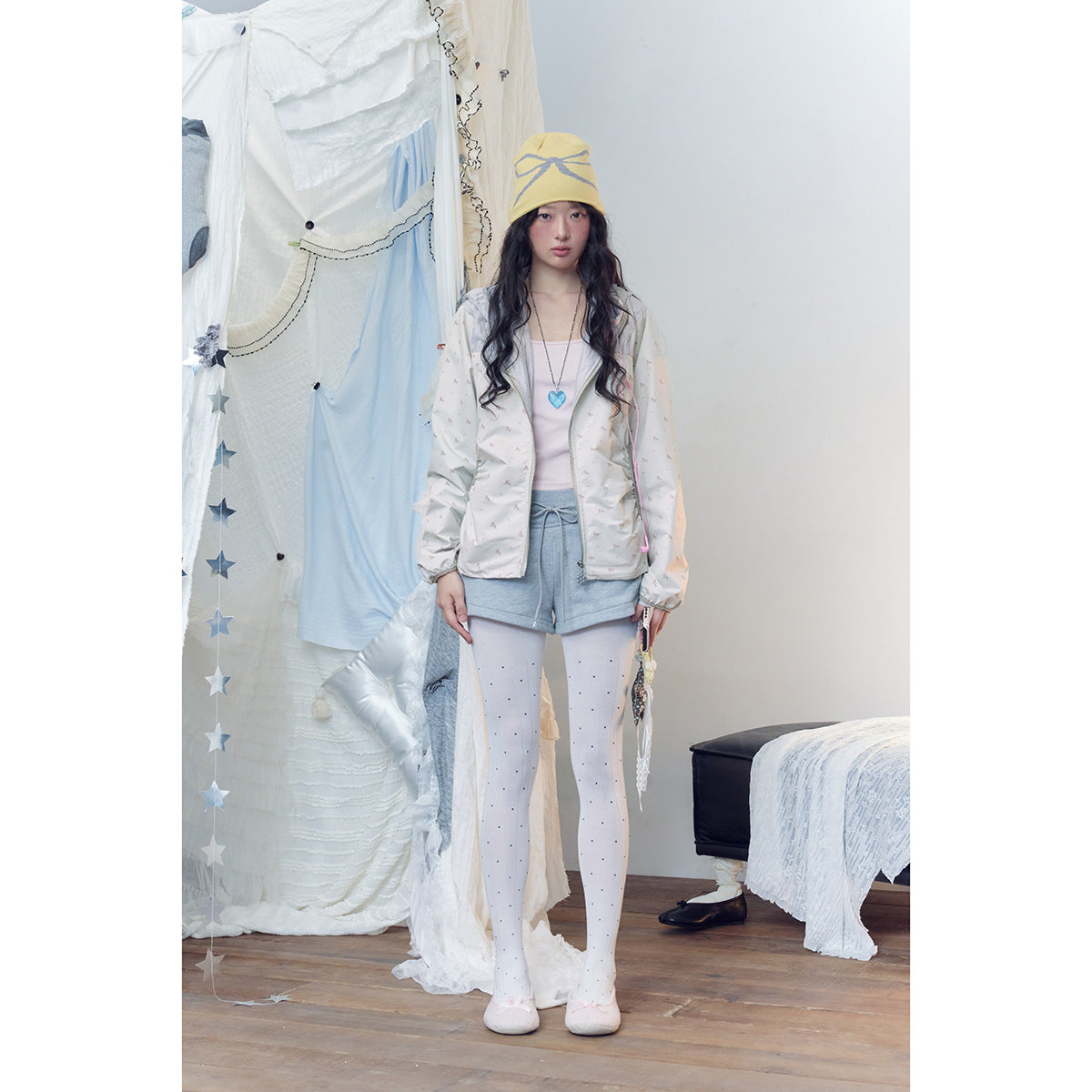 Front view of a model wearing an off-white printed hooded jacket with gray shorts and dotted white tights.