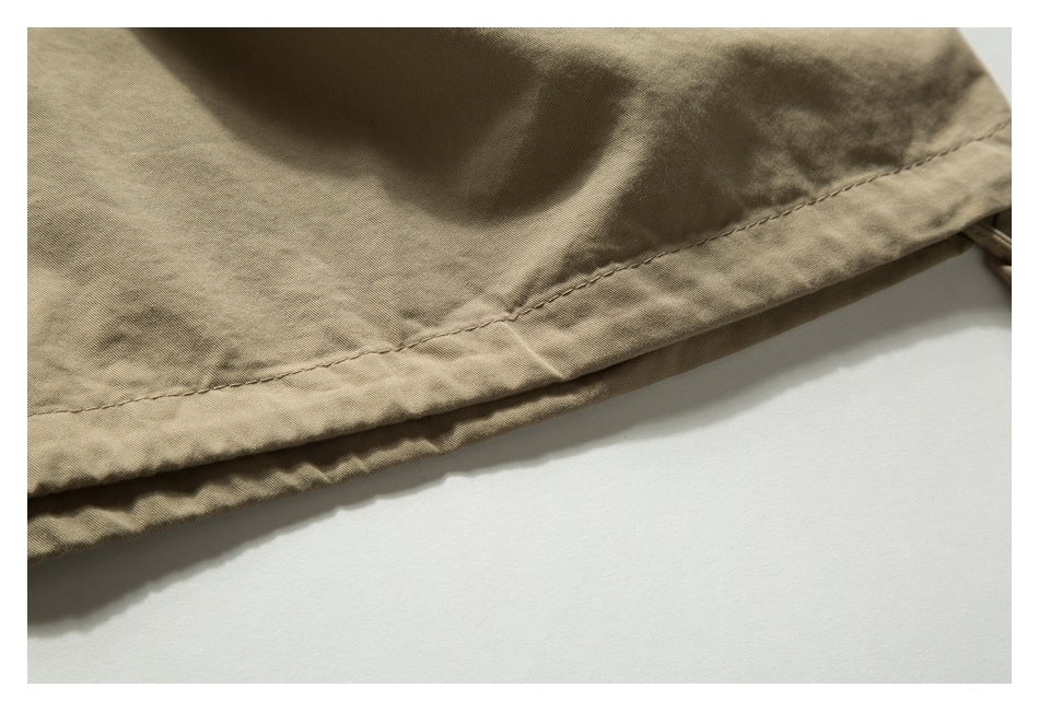 Close-up of the stitched hem on tan trousers against a white background.