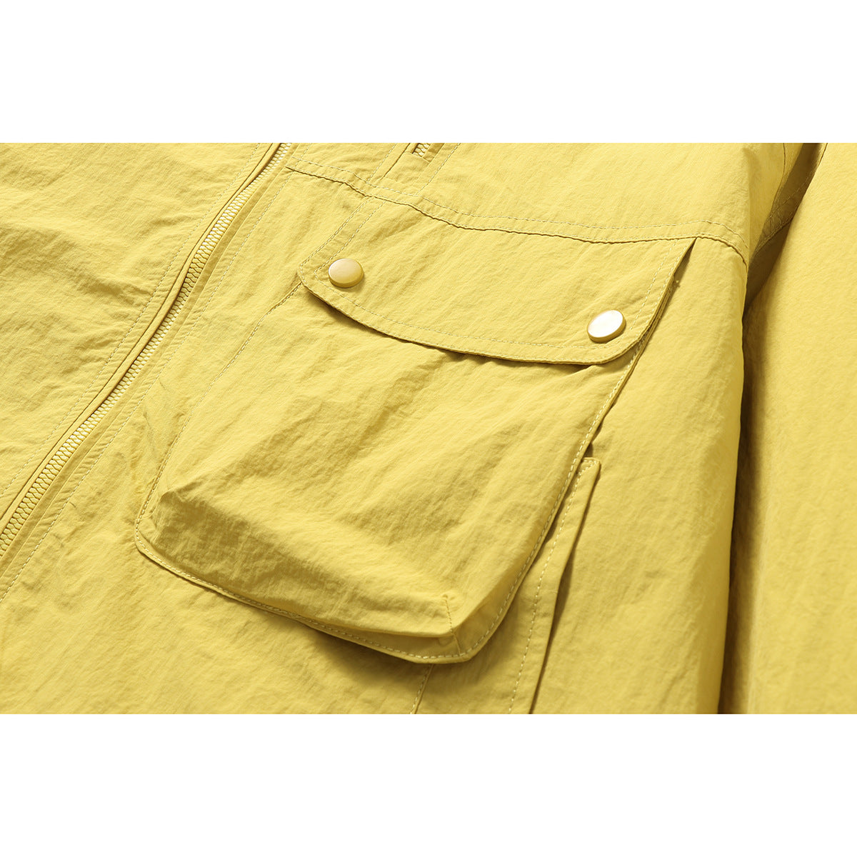 Close-up of a yellow jacket's large flap pocket with two snap buttons and a nearby zipper.