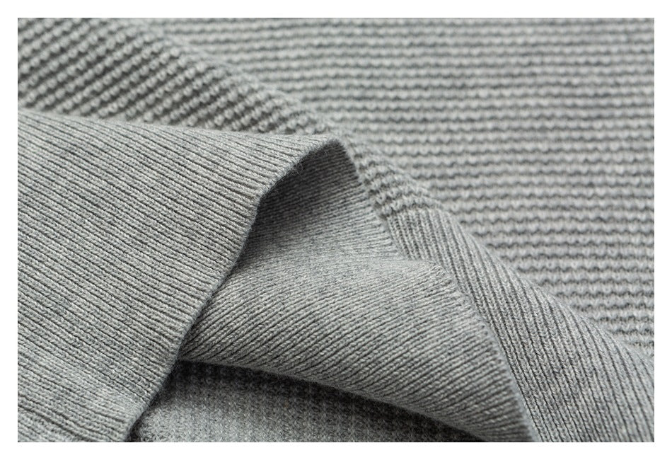 Close-up of a ribbed edge folded over the light gray sweater’s textured knit.