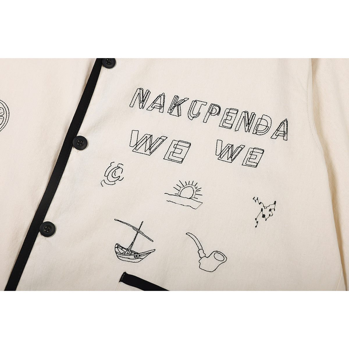 Close-up of outlined lettering and small illustrations on the chest of a cream shirt with black buttons and piping.