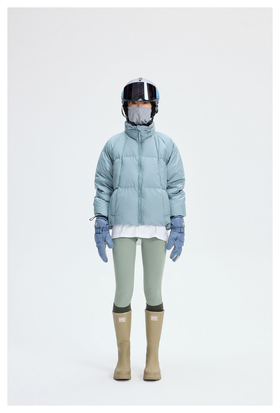 Full-length front view of a person wearing a pale blue puffer jacket, sage leggings, gloves, and tan boots.