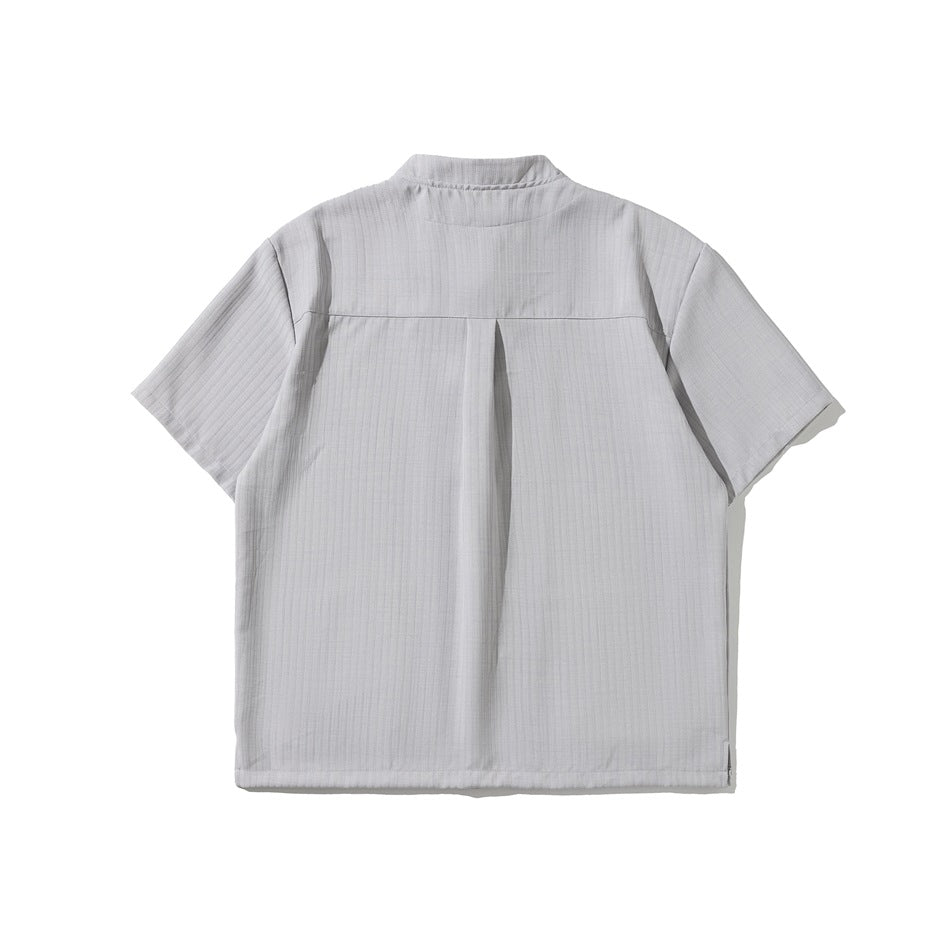 Back view of light gray short-sleeve shirt with stand collar, back yoke, center pleat and side hem vents, flat lay