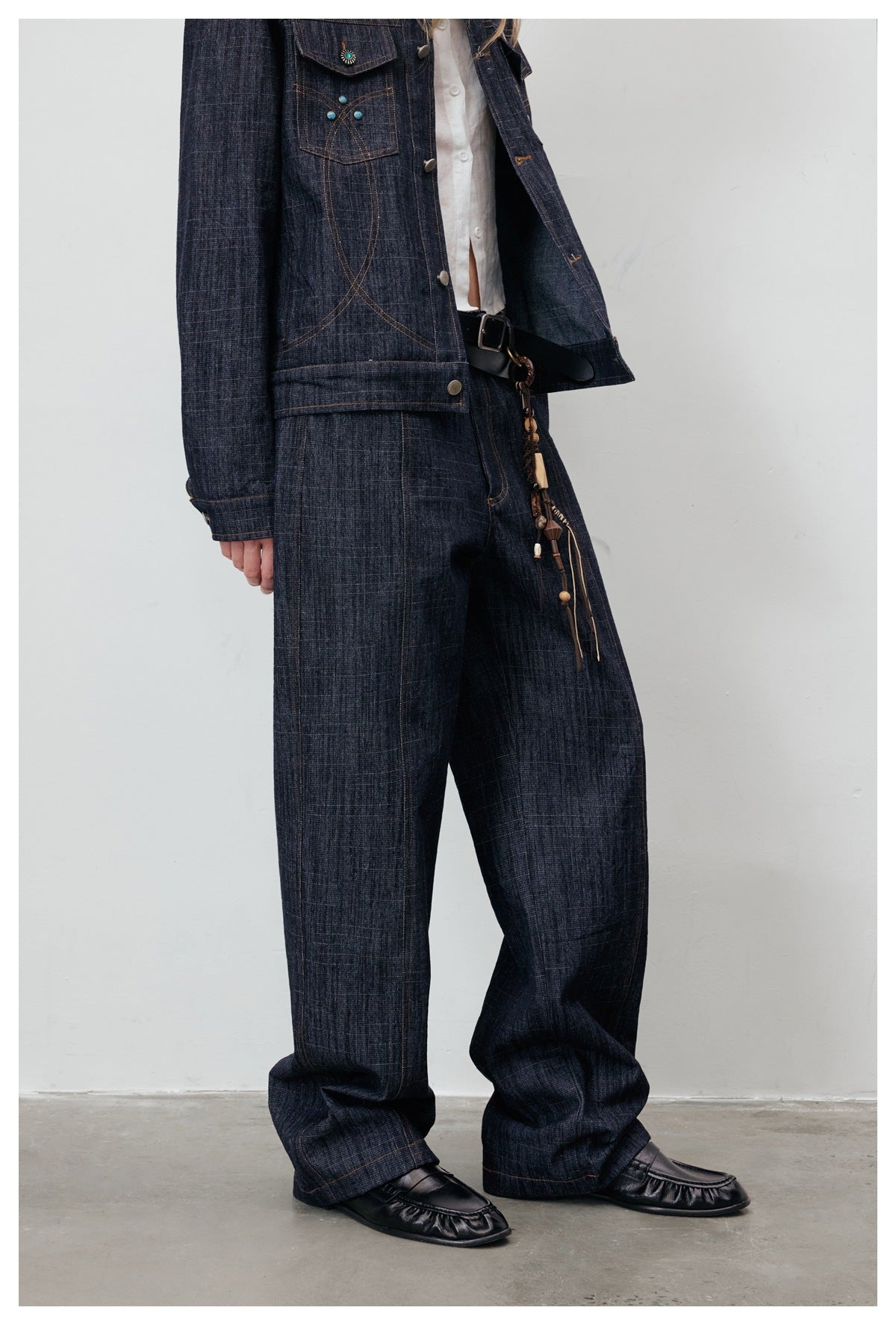 Model wearing dark wide-leg denim jeans with matching jacket, black belt and black loafers, three-quarter view