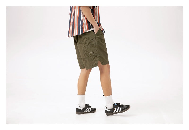 Side view of a model wearing olive-green knee-length shorts with a pocket and side slit.