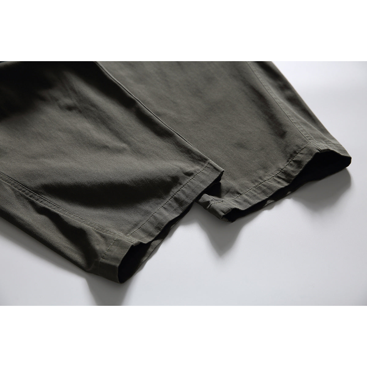 Close-up of both dark olive pant legs and their stitched hems.