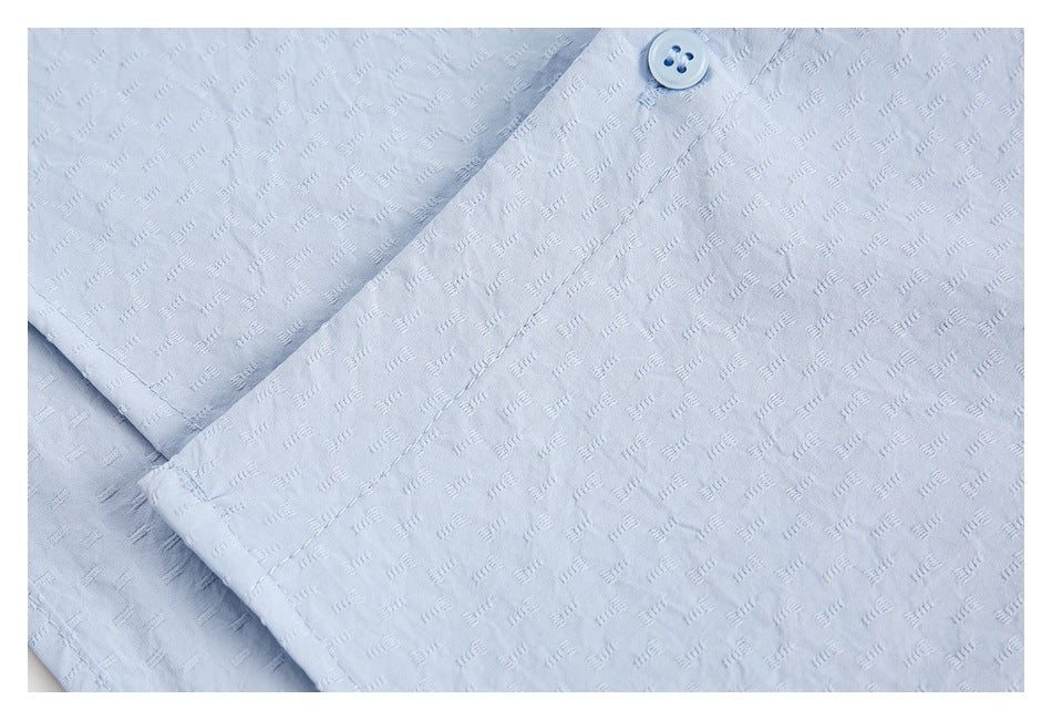 Close-up of pale blue patterned shirt fabric with a matching button and stitched placket.