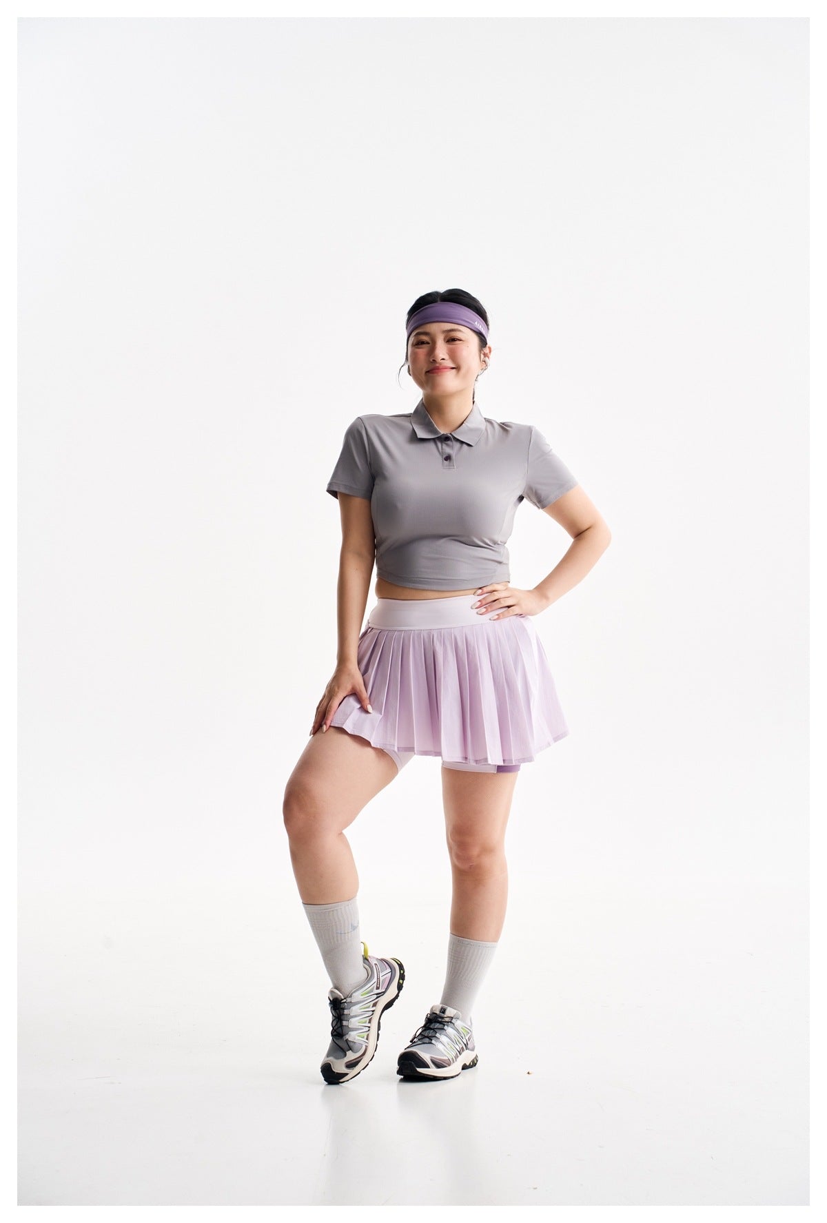 Model wearing a gray cropped polo shirt and lilac pleated athletic skirt with built-in shorts.