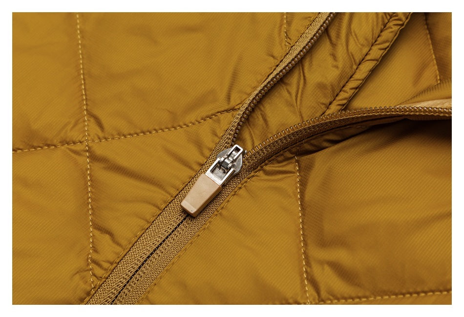 Close-up of a tan zipper and pull on mustard-gold padded jacket fabric with stitched panels.