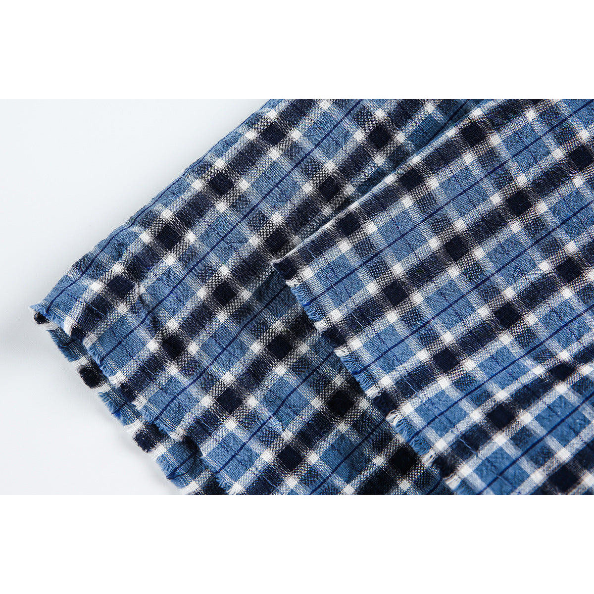 Close-up of the frayed edge and stitching on blue, black, and white plaid fabric.
