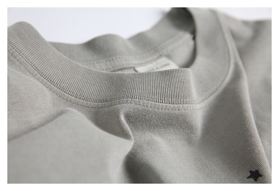 Close-up of the gray T-shirt’s ribbed crew neck, stitching and a small star from its print.