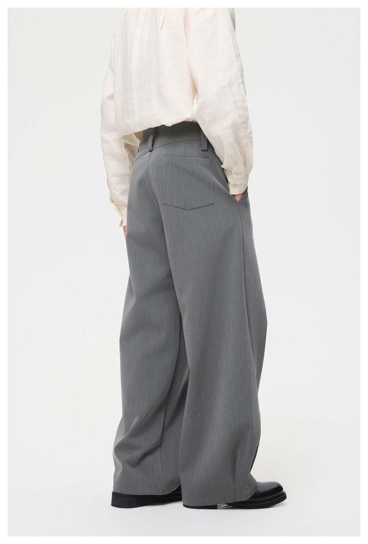 Rear view of a model wearing gray wide-leg trousers with belt loops and a back pocket, styled with an ivory shirt.