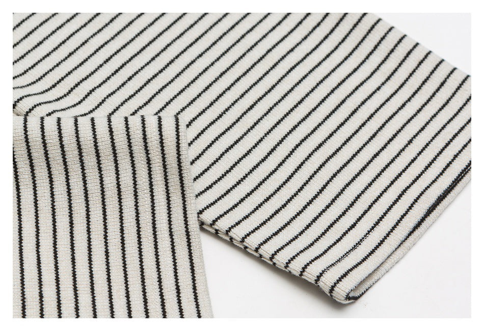 Close-up of the cream shirt’s dark stripes and finished sleeve cuff, with fabric folded to show the seam.