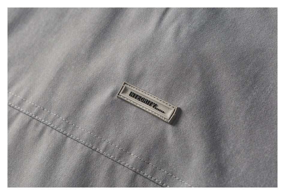 Close-up of gray jacket fabric with a small rectangular metal badge reading “INTEGRITY.”