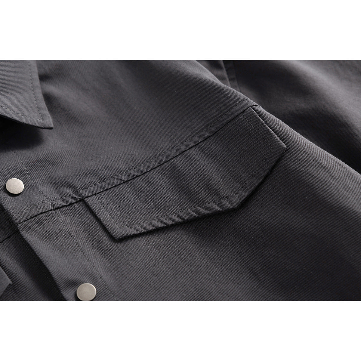 Close-up of a charcoal shirt's flap chest pocket, stitching, and metal snap buttons.