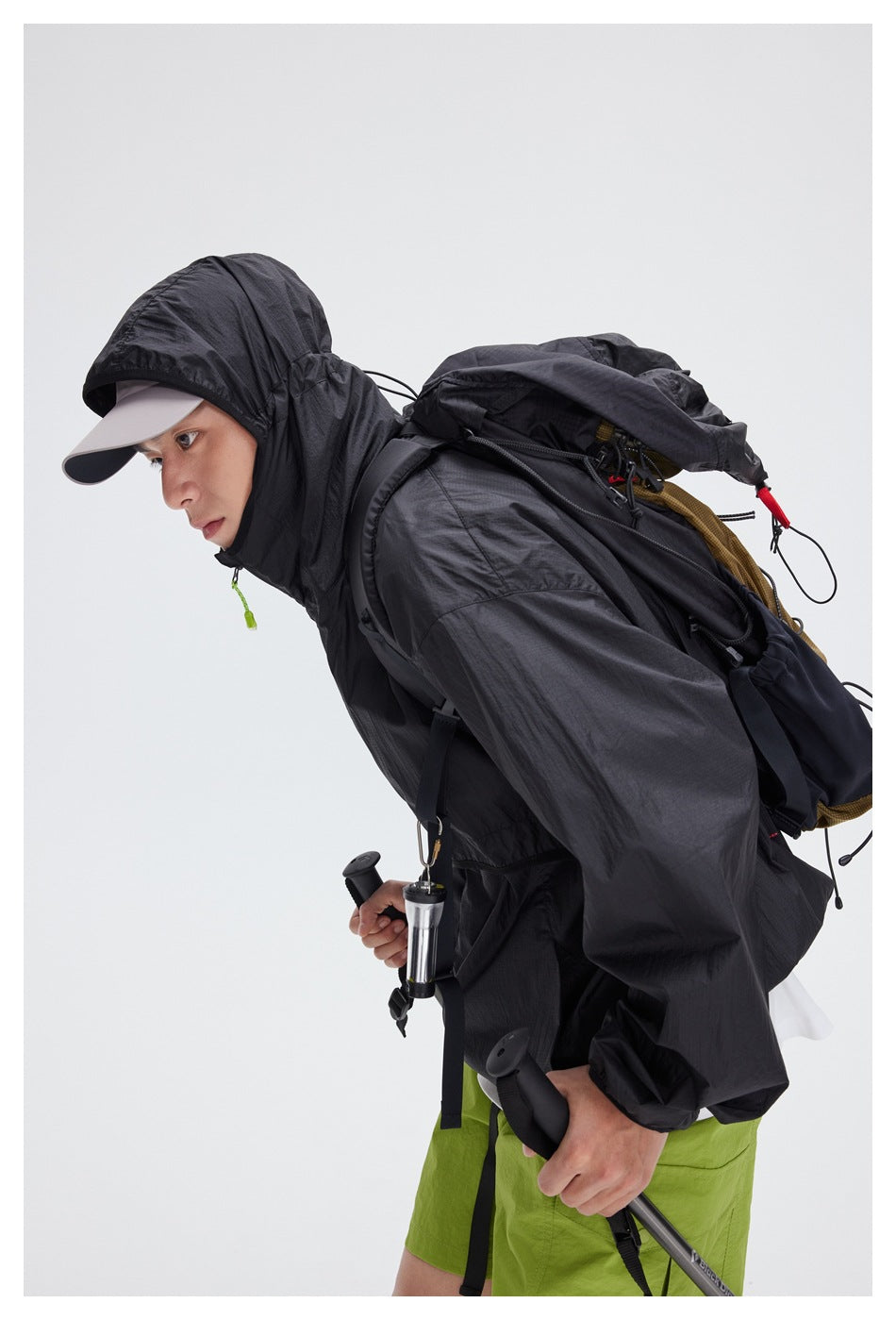 Close side view of a model wearing a black hooded jacket with a backpack and lime-green shorts.