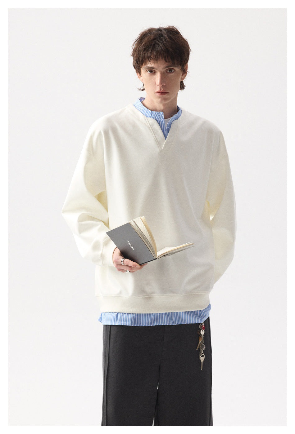 Model wearing a cream V-neck sweatshirt over a blue striped shirt, shown from head to upper legs.