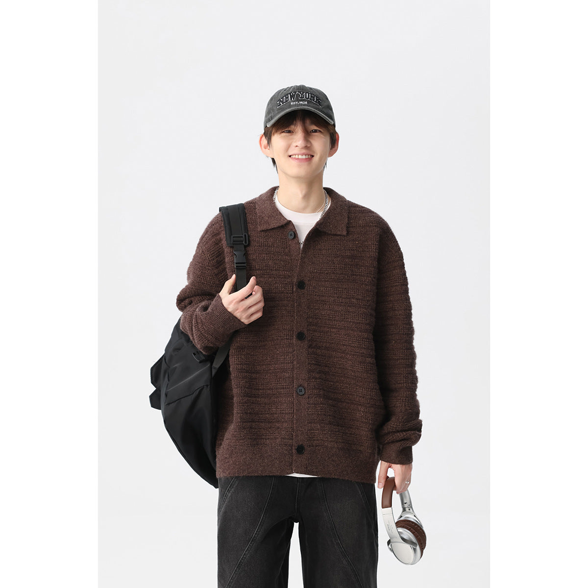 Model wearing a brown textured knit cardigan with a collar and dark buttons, styled with a cap and black bag.