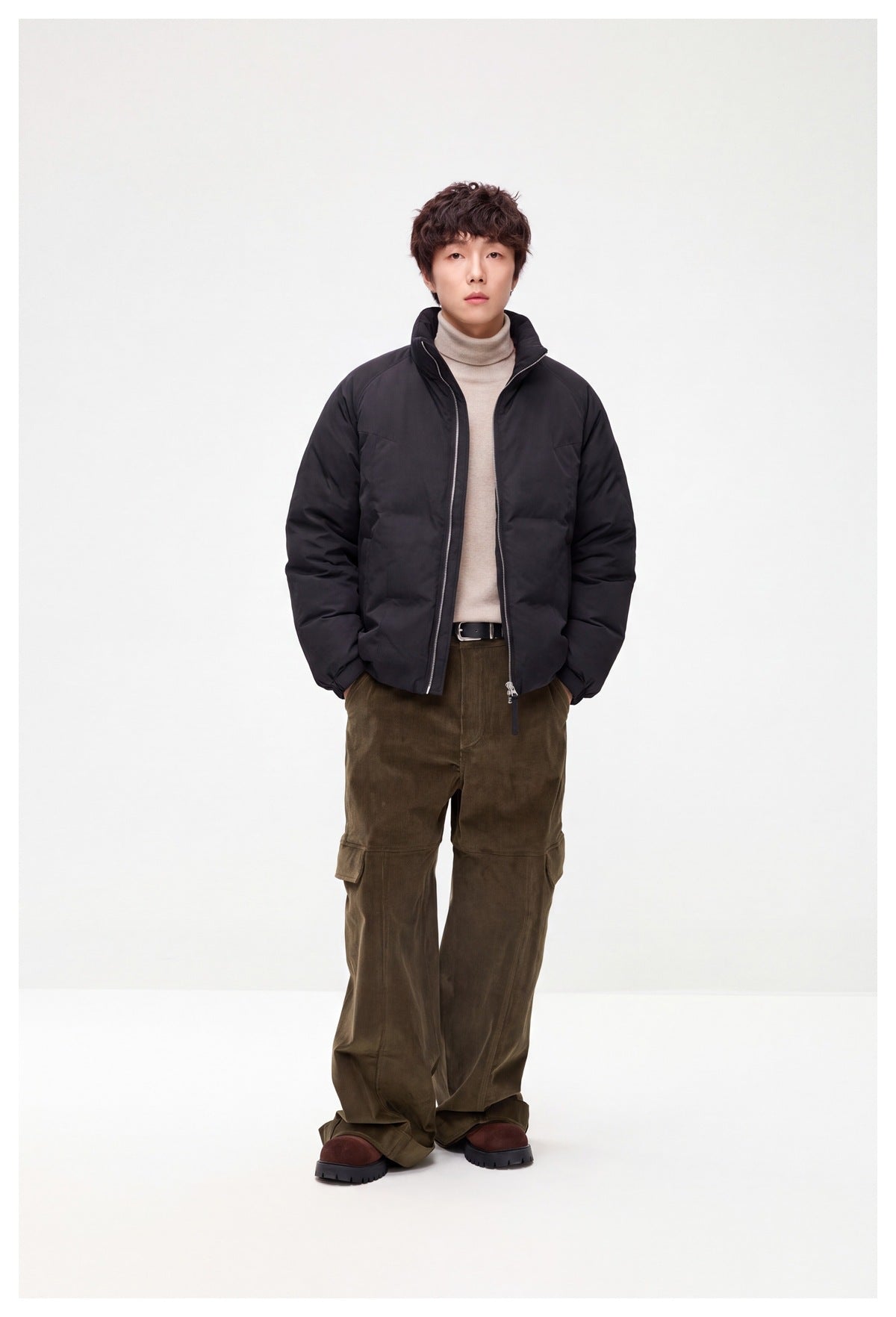 Front view of a model wearing a black zip-front jacket with a raised collar and olive cargo trousers.