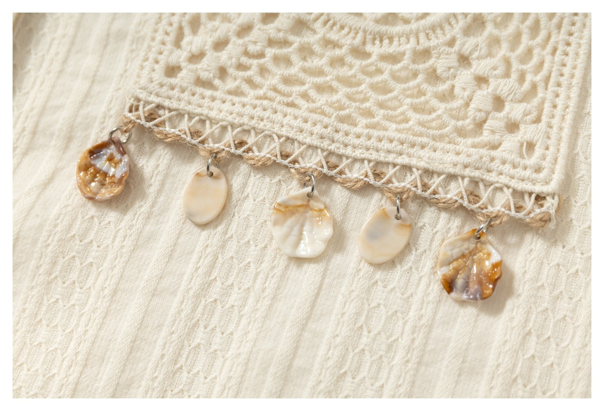 Close-up of an ivory garment with a crocheted edge and five cream and amber shell-shaped hanging embellishments.