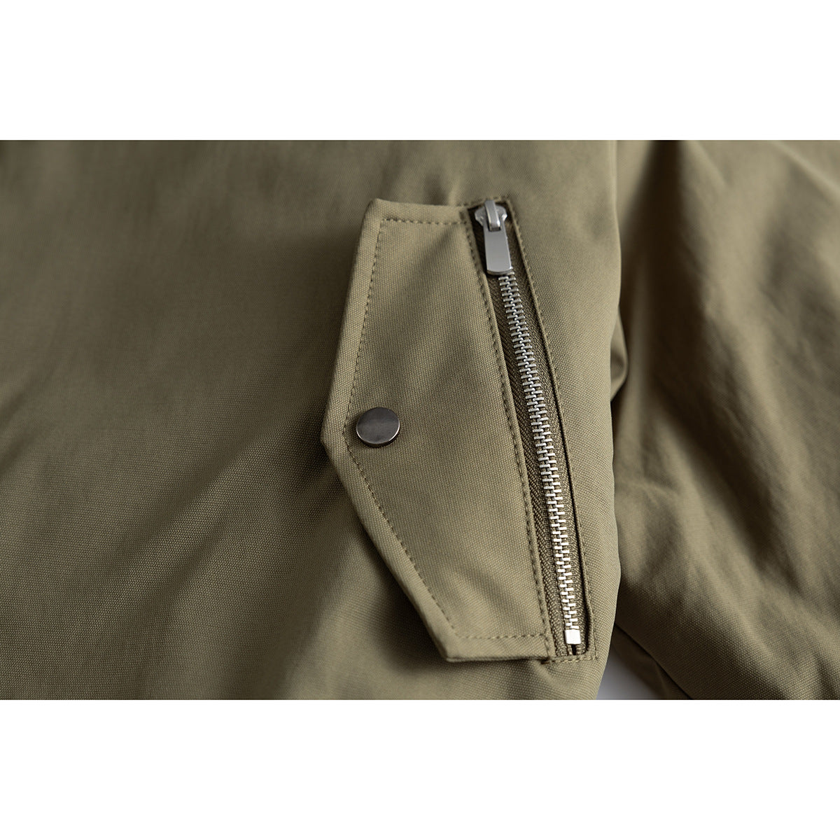 Close-up of an olive jacket's side zipper pocket with a snap-button flap.