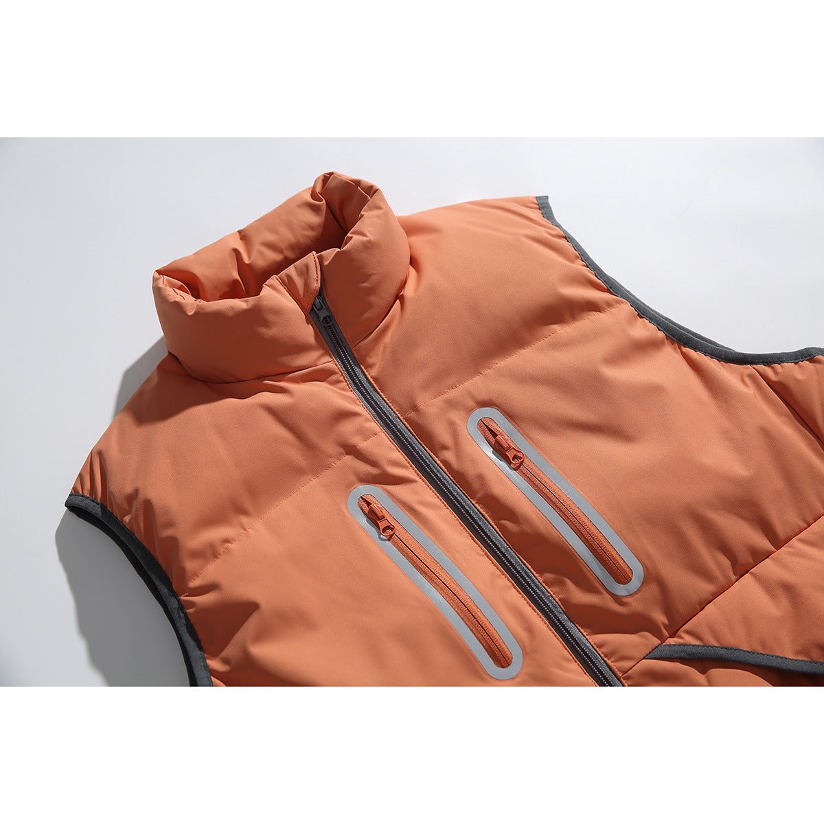 Close-up of a rust-orange padded vest showing its high collar, dark center zipper, and reflective-trimmed chest pockets.