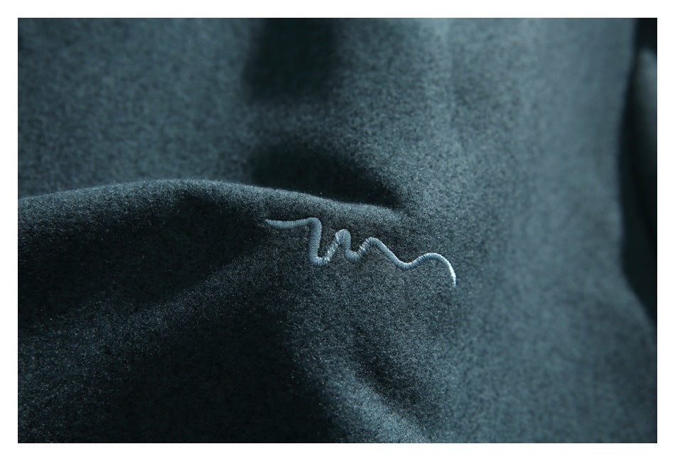 Close-up of a small curved embroidered mark on dark teal fabric.