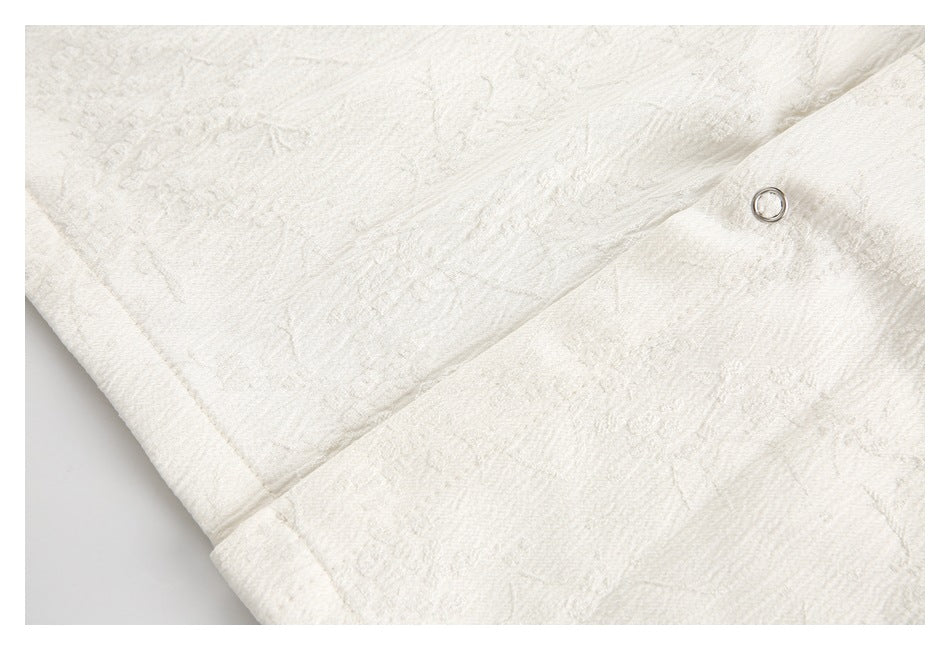 Close-up of ivory textured fabric with a seam, raised foliage pattern, and a metal ring closure.