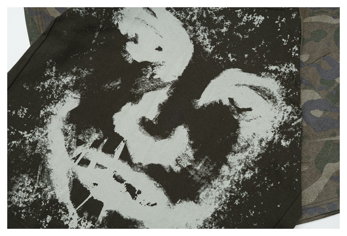 Close-up of a dark olive shirt with a large distressed white graphic; camouflage fabric is visible behind it.